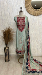 Light green embroidered dress with red and blue patterns on a mannequin against a textured wall.