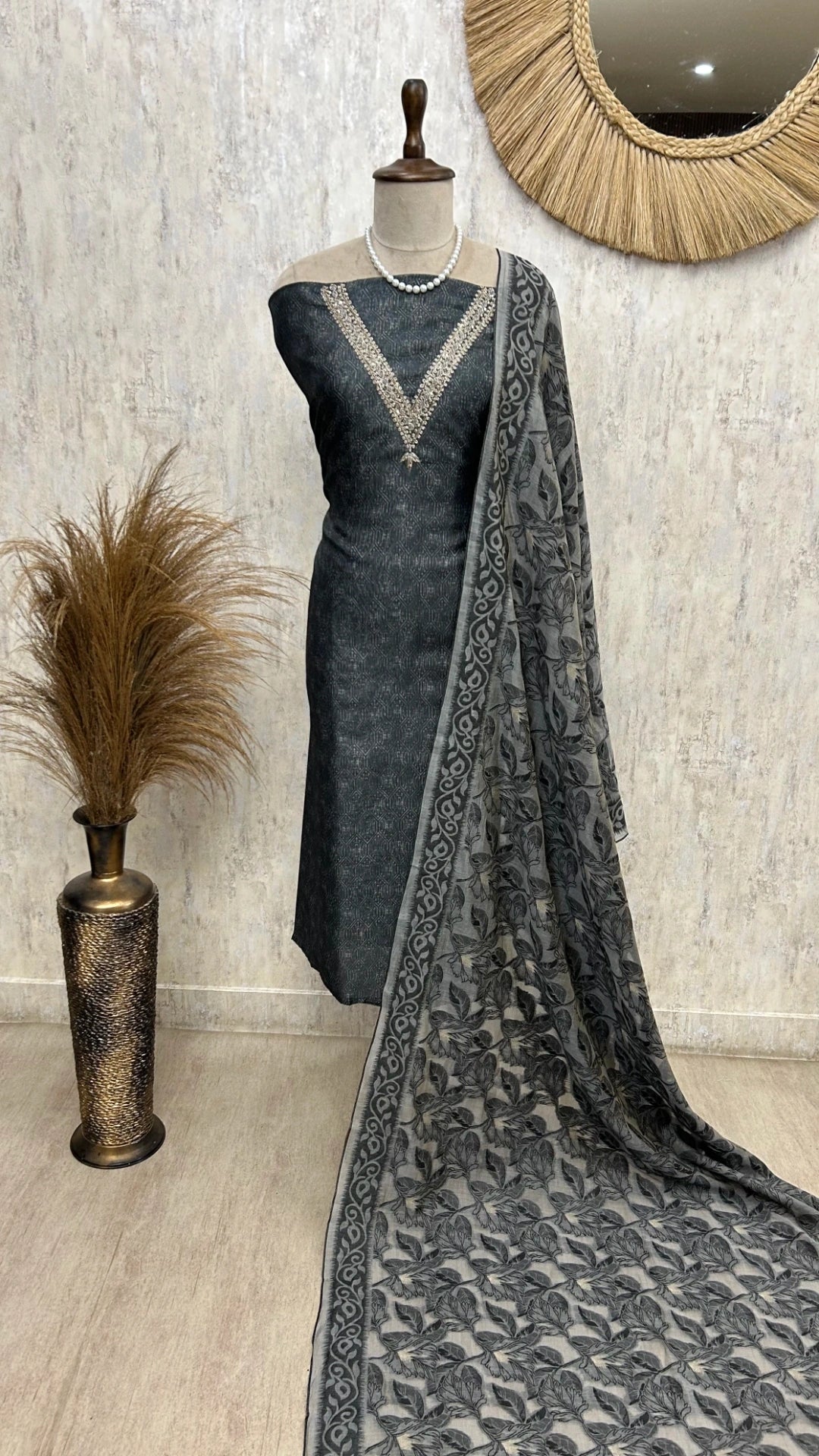 Gray saree with a patterned border on a mannequin against a textured wall.