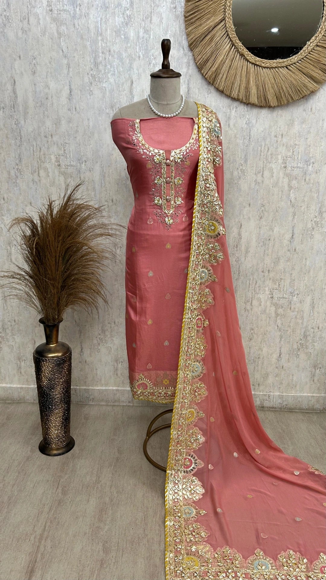 Pink saree with gold border on a mannequin against a neutral wall.