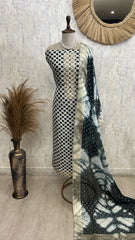 Mannequin wearing a black and white patterned dress with a tie-dye fabric draped over it, against a textured wall.