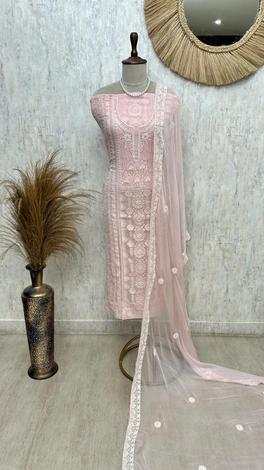 Mannequin wearing a light pink embroidered outfit with a sheer dupatta in a room setting.