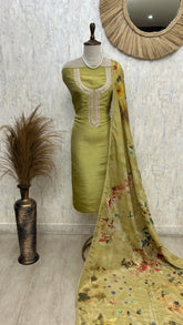 Green embroidered dress with floral dupatta on a mannequin against a textured wall.
