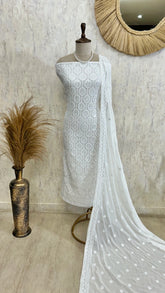 White embroidered dress on a mannequin with a textured wall and decorative mirror in the background