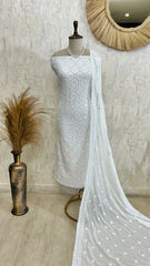 White embroidered dress on a mannequin with a textured wall and decorative mirror in the background