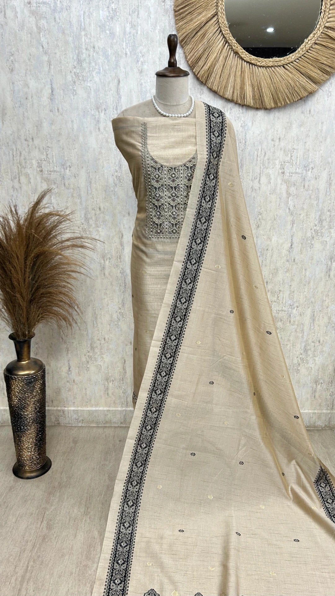 Mannequin wearing a cream saree with black border against a textured wall.