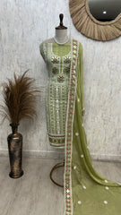 Green embroidered traditional outfit on a mannequin against a textured wall.