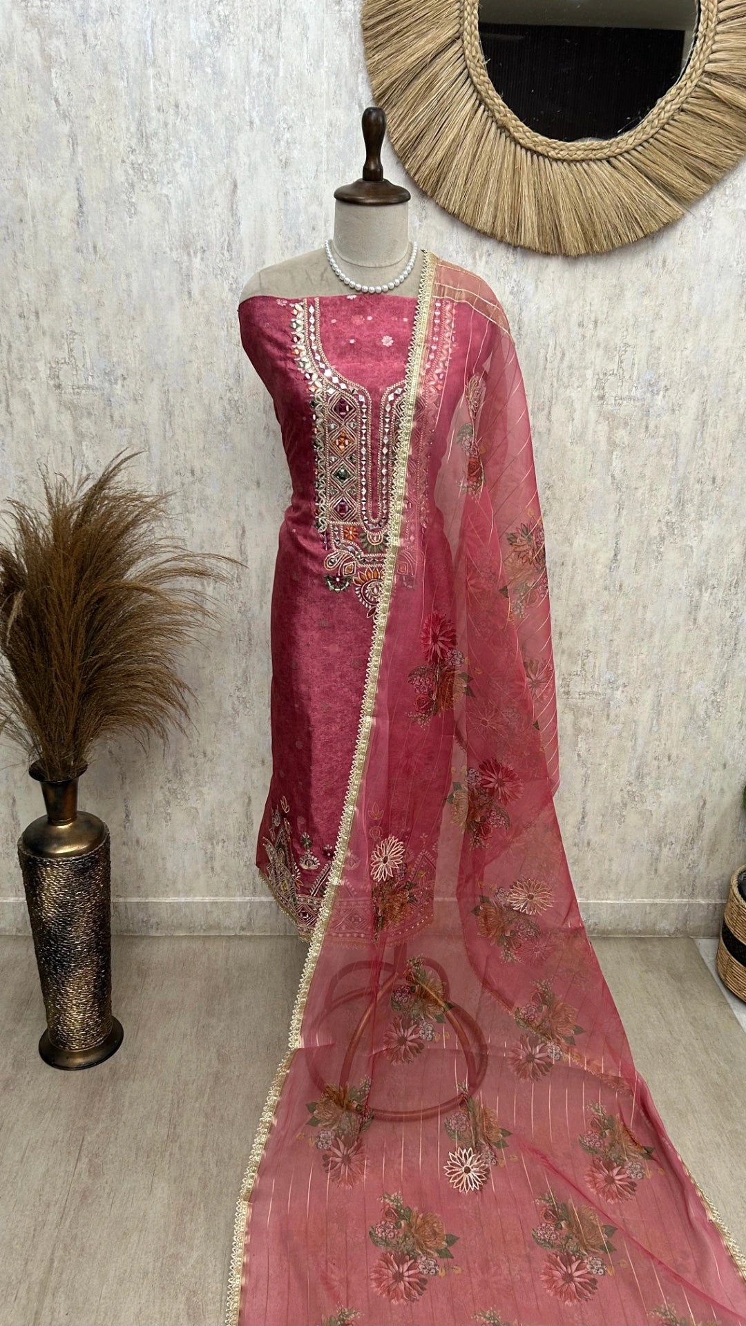 Pink embroidered traditional outfit on a mannequin against a textured wall.