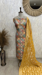 Mannequin wearing a patterned dress with a yellow dupatta against a textured wall.