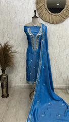 Blue embroidered traditional outfit on a mannequin against a textured wall.