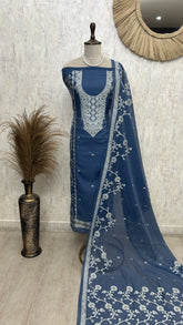 Blue embroidered suit on a mannequin against a textured wall.