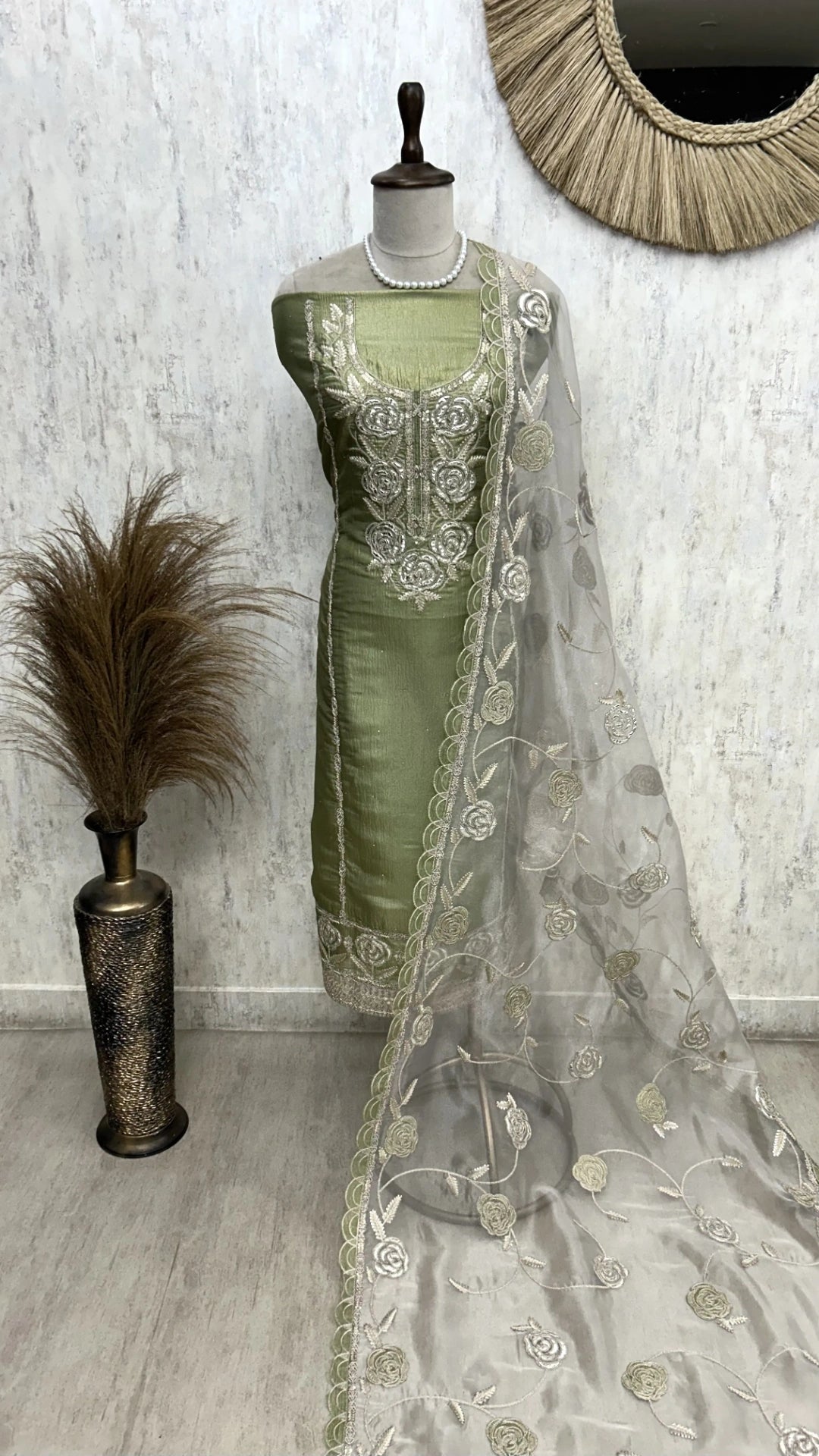 Green saree with silver embroidery on a mannequin against a white wall.
