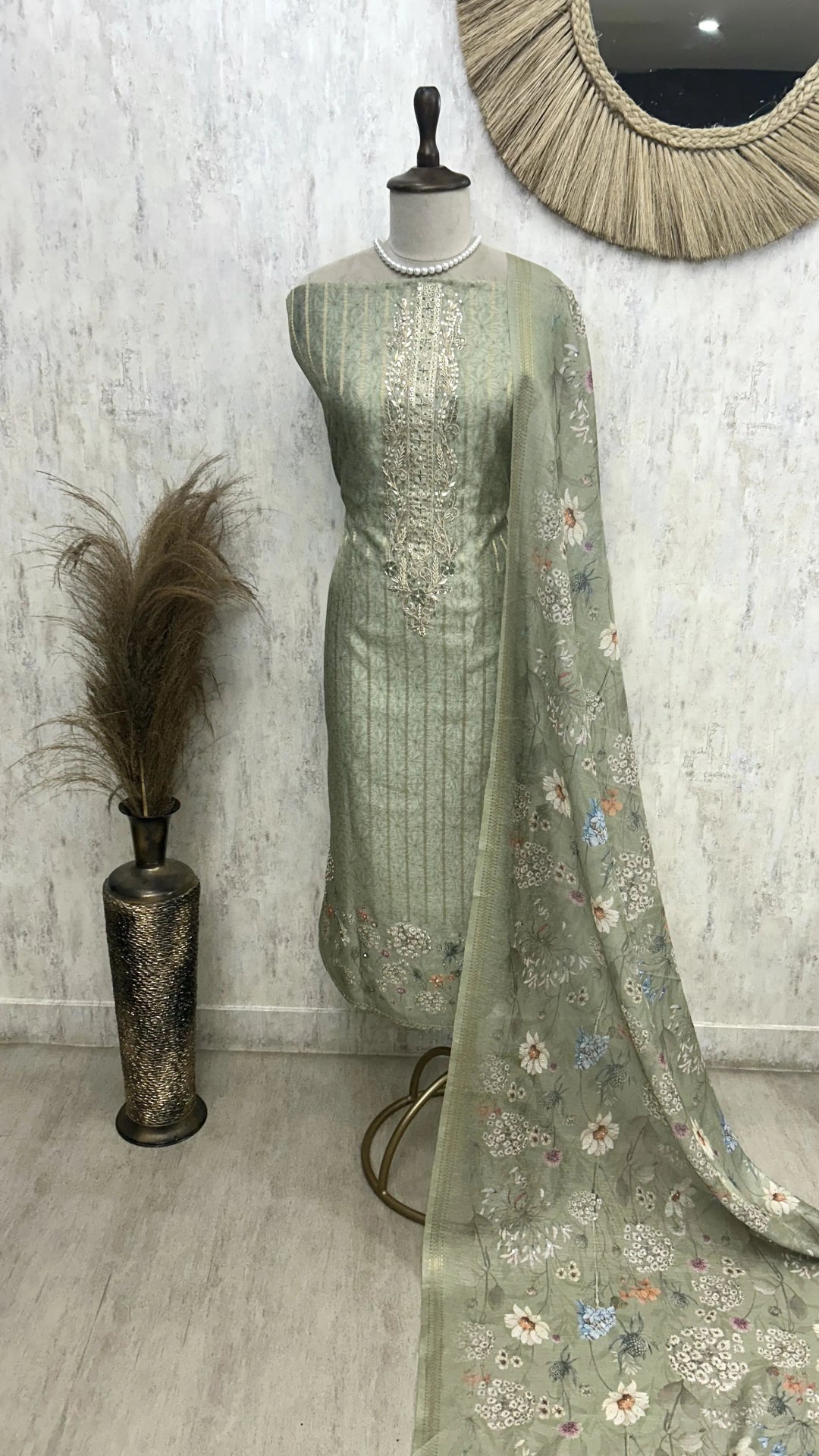 Green embroidered traditional outfit on a mannequin against a white wall.