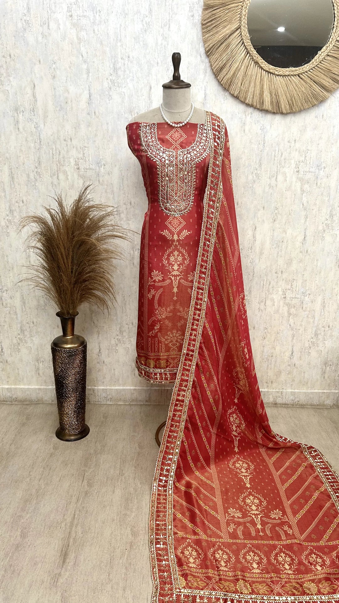 Red embroidered traditional outfit with a matching dupatta on a mannequin against a neutral wall.