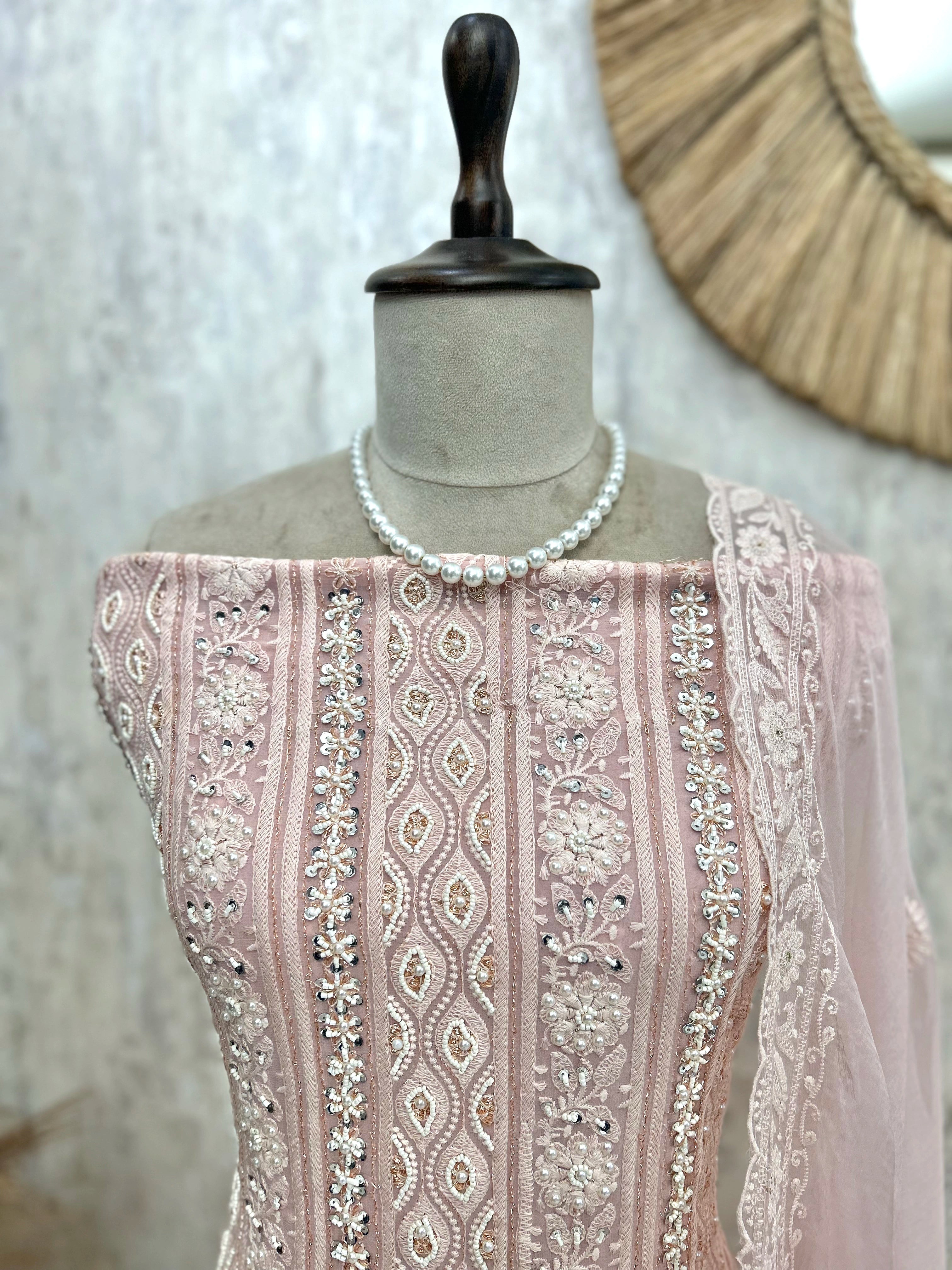 Mannequin wearing a pink embroidered garment with a pearl necklace against a neutral background