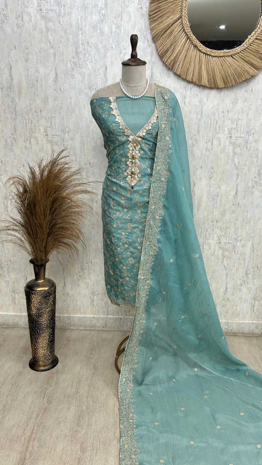 Teal embroidered dress with matching dupatta on a mannequin against a neutral wall.