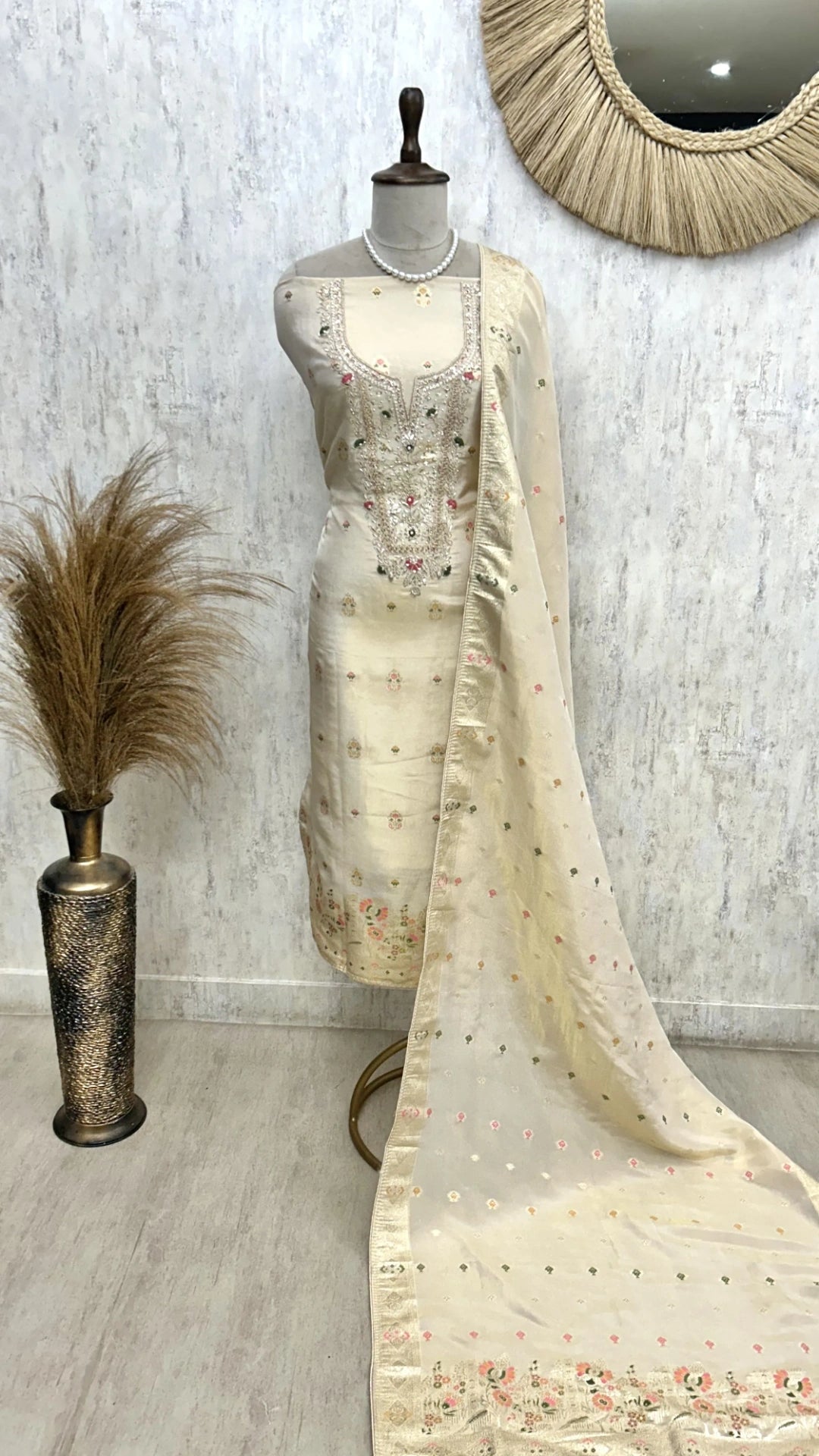 Mannequin wearing a cream saree with floral patterns against a light gray wall.