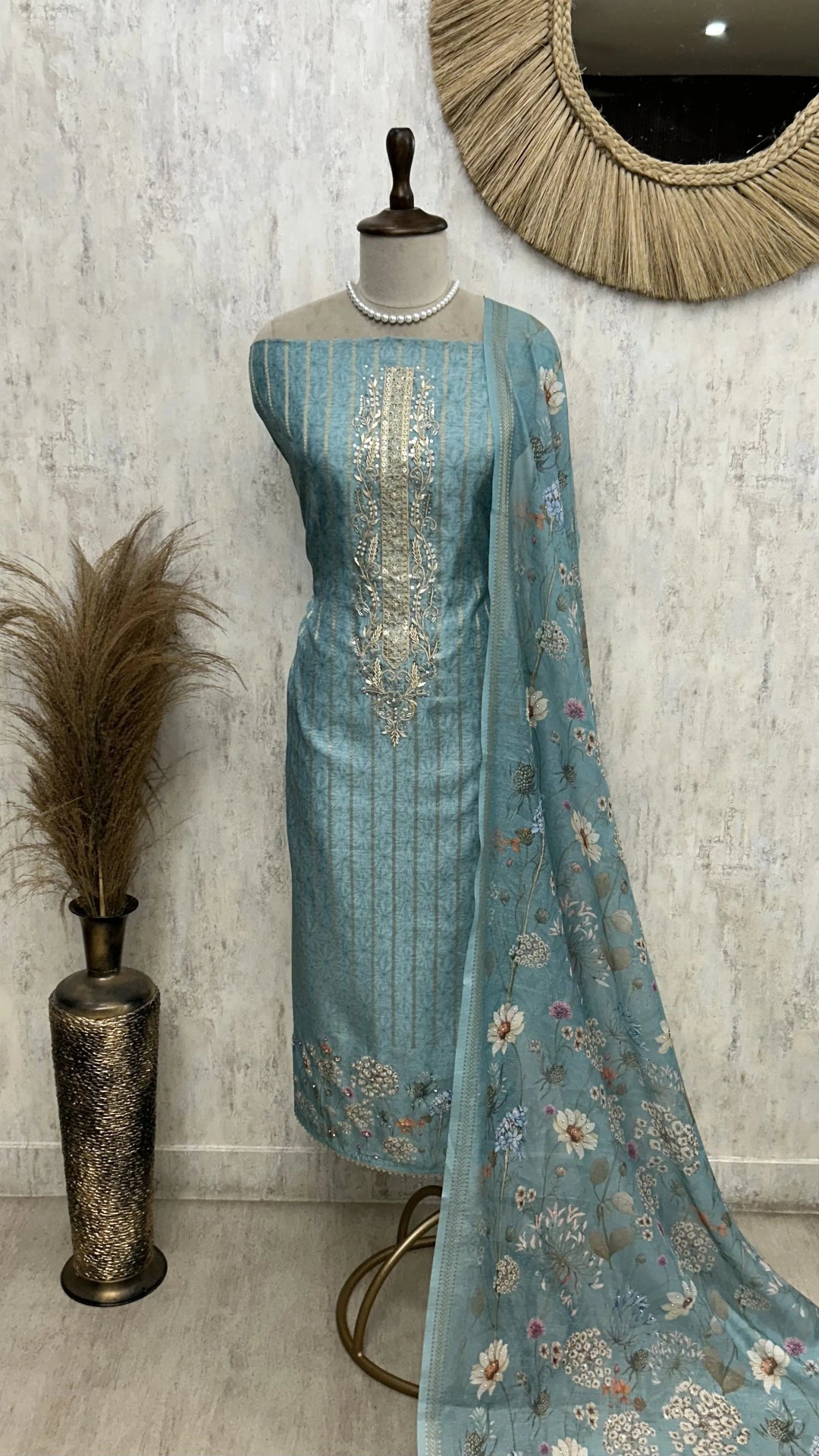 Teal embroidered saree with a matching blouse on a mannequin against a textured wall.